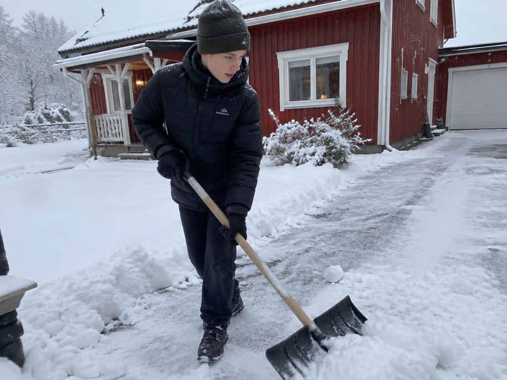 En ungdom skakar snö utanför ett rödmålat hus